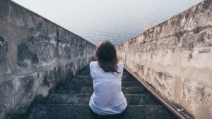 Isolated woman sitting on stairs staring at ocean, seeming depressed